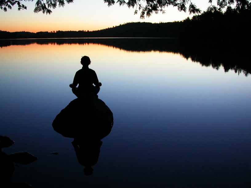 a pic of someone meditating beside a calm lake for their emotional eating treatment